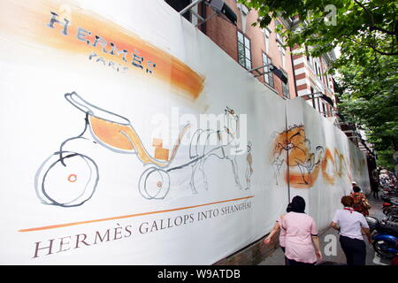 Lokale chinesische Bewohner vorbei an einer Werbung für Hermes außerhalb der Hermes Villa im Stadtbezirk Luwan in Shanghai, China, 9. August 2010. Französisch Stockfoto