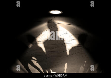 Gruppe von Menschen, Silhouetten und Schatten an der Wand, Licht der Lampe oder Flutlicht auf der alten Mauer mit Schatten, Konzept Bild Stockfoto