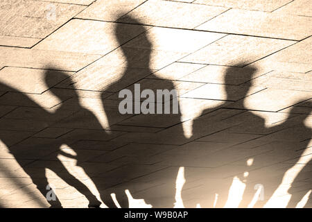 Menschen, Schatten und Silhouetten, die auf dem Bürgersteig, Gehweg im Morgen, Lichter, als Hintergrund- oder Textur, Konzept Bild Stockfoto