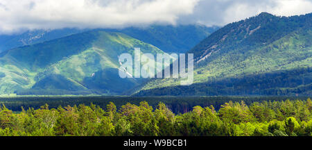 Die Sonnenstrahlen scheinen durch schwere Wolken fließt Tief über die bewaldeten Bergrücken und ein Highland Valley an einem Sommernachmittag. Altai Gebirge, Kasachen Stockfoto