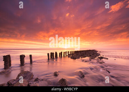 Schönen roten Sonnenuntergang am Meer mit Felsen und einem dramatischen Himmel im Vordergrund - Reisen Bild - Wattenmeer Stockfoto