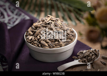 Eine Schüssel gefüllt mit gerösteten Sonnenblumenkernen auf einem dunklen, eleganten Hintergrund, die eine gesunde Snackoption bietet Stockfoto