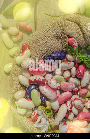 Sack von mix Bohnen verschütten Bohnen mit Bohnen auf Holztisch. Lima Bohnen in sackleinen Beutel auf Holz- Hintergrund. Stockfoto