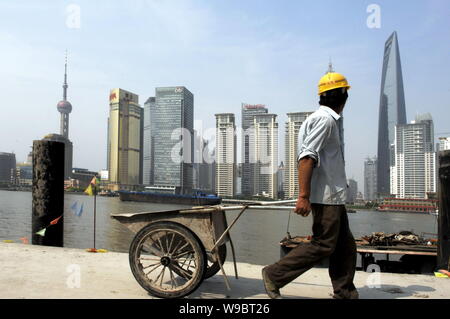 ---- Ein chinesischer Wanderarbeiter zieht eine Karre auf einer Baustelle auf dem Bund als die Landschaft der Lujiazui Financial District mit der Orientalischen Stockfoto