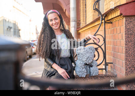 Hübsche Frau, die zu Fuß in die Stadt mit grauen Teddybär von foamirane Rosen. Stockfoto