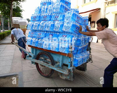 ---- Ein chinesischer Wanderarbeiter zieht einen Warenkorb mit Hunderten von Wasserflaschen geladen und wird von einem anderen Mitarbeiter, gesehen wird, Peking, China, Octob unterstützt. Stockfoto