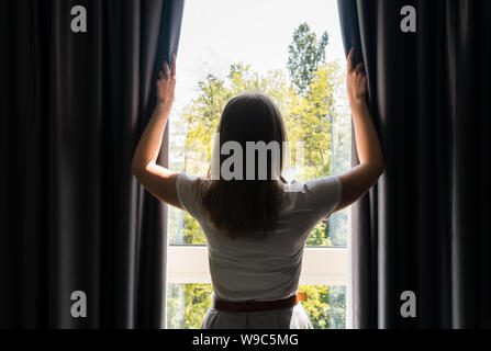 Frau Eröffnung Vorhänge in das Zimmer am Morgen. Stockfoto