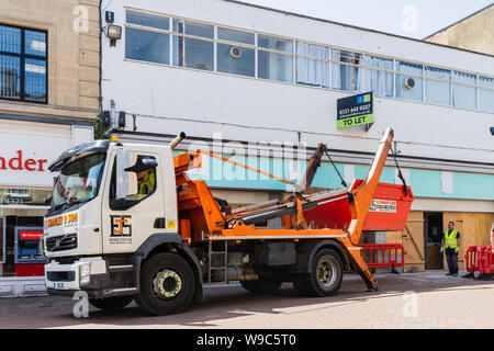 Ein überspringen Lkw von einem Shop unter Sanierung, mit dem Fahrer über die Steuerelemente zu heben ein Überspringen von Gebäude Abfälle auf die Lkw, in Chippenham Wiltshire Stockfoto