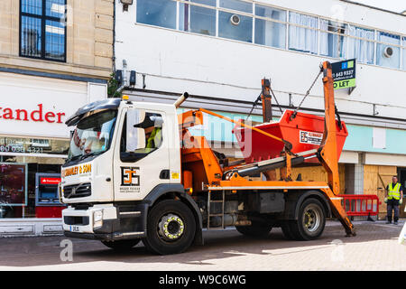 Ein überspringen Lkw von einem Shop unter Sanierung, mit dem Fahrer über die Steuerelemente zu heben ein Überspringen von Gebäude Abfälle auf die Lkw, in Chippenham Wiltshire Stockfoto