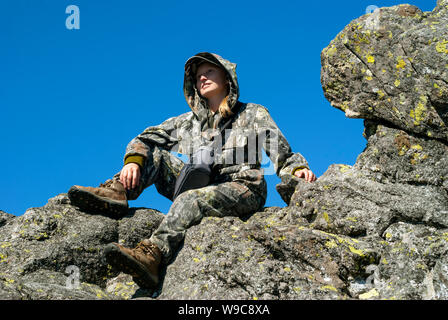 Lächelnd Wanderer Mädchen in die Ferne suchen, saß oben auf einer Klippe. Stockfoto