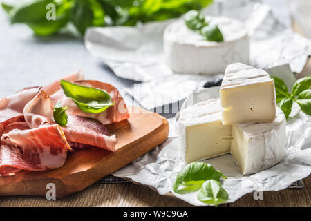 Camembert oder Brie Käse und Schweinefleisch Schinken Prosciutto mit basilikumblätter auf Tisch Stockfoto
