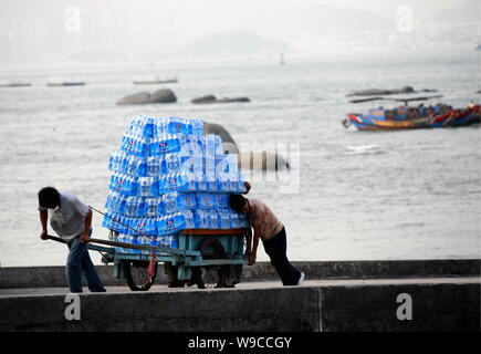 ---- Ein chinesischer Wanderarbeiter zieht einen Warenkorb mit Hunderten von Wasserflaschen geladen und wird von einem anderen Mitarbeiter, gesehen wird, Peking, China, Octob unterstützt. Stockfoto