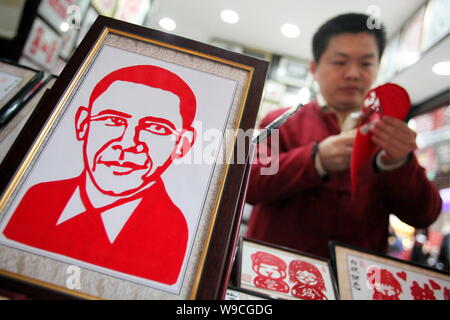 Ein Chinesisches Geschäft Inhaber ist gesehen, eine Papier-cut Arbeiten neben einer Papier-cut Arbeit der Portrait von US-Präsident Barack Obama an seine Papier-cut Shop in Stockfoto