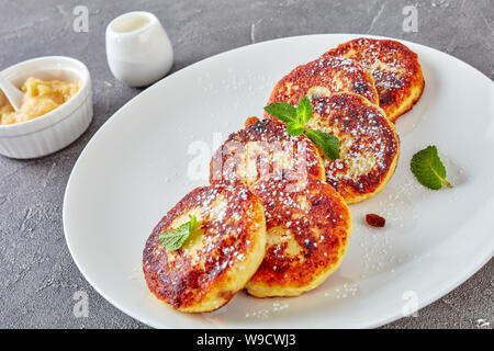 Close-up der Deutschen quark Kartoffelpuffer - Quarkkeulchen mit Puderzucker bestreut, mit Minze auf eine weiße Platte mit Apfelmus eingerichtet, Stockfoto