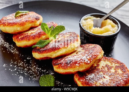 Close-up der Deutschen quark Kartoffelpuffer - Quarkkeulchen mit Puderzucker bestreut, mit Minze auf einer schwarzen Platte mit Apfelmus eingerichtet, Stockfoto