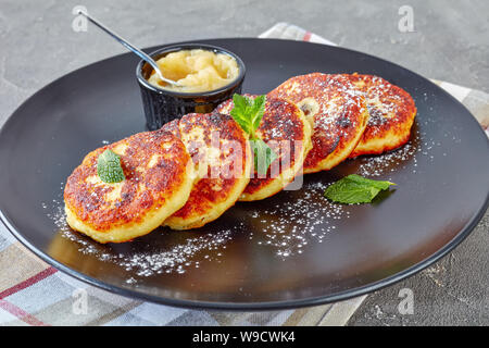 Close-up der Deutschen quark Kartoffelpuffer - Quarkkeulchen mit Puderzucker bestreut, mit Minze auf einer schwarzen Platte mit Apfelmus eingerichtet, Stockfoto