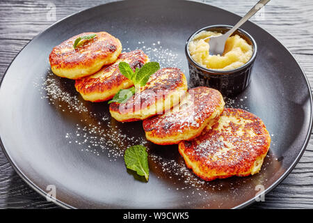 Close-up der Deutschen quark Kartoffelpuffer - Quarkkeulchen mit Puderzucker bestreut und mit Minze auf einer schwarzen Platte mit Apple sa eingerichtet Stockfoto