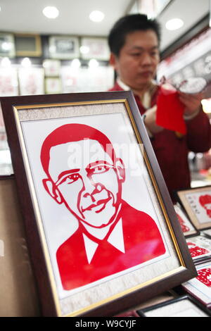 Ein Chinesisches Geschäft Inhaber ist gesehen, eine Papier-cut Arbeiten neben einer Papier-cut Arbeit der Portrait von US-Präsident Barack Obama an seine Papier-cut Shop in Stockfoto