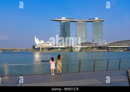 Chinesische Touristen auf Fußgänger Jubilee Bridge für Fotografien mit Marina Bay und die Ikonischen Marina Bay Sands Hotel in der b/g posiert; Singapur Stockfoto