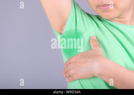 Close-up junge Frauen mit Hyperhidrose schwitzen. Junge Frau mit Schweiß Flecken auf Ihrer Kleidung vor grauem Hintergrund. Healthcare Konzept. Stockfoto