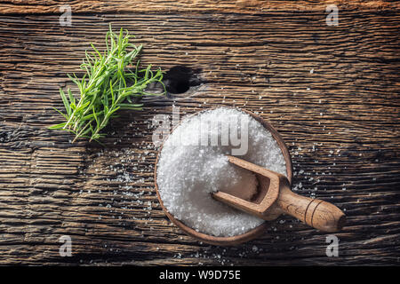 Grobkörniges Salz mit Rosmarin Kräuter in eine hölzerne Schüssel mit einer Schöpfkelle auf einer alten Eiche Tisch Stockfoto