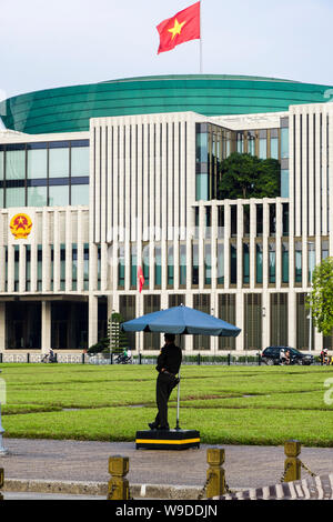 Eine vietnamesische Soldaten im Schatten unter einem Sonnenschirm steht auf Wache außerhalb der Nationalversammlung Haus Parlamentsgebäude. Hanoi, Vietnam, Asien Stockfoto