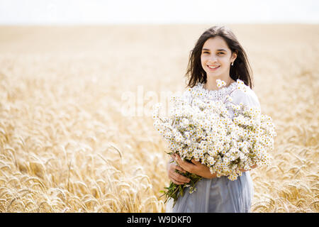 Recht jugendlich Mädchen stehen in einem Feld unter den Weizen. Mädchen, dass einen großen Strauß Blumen Stockfoto