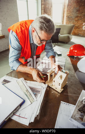 Close up photoshot der männlichen Architekt - Ingenieur ein Modell der Zukunft Haus für die junge Familie. Mann bei der Arbeit im Büro mit Miniatur, Zeichnungen, Blaupause. Erstes Haus, Industrie, Gebäude Konzept. Stockfoto