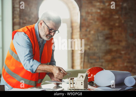 Close up photoshot der männlichen Architekt - Ingenieur ein Modell der Zukunft Haus für die junge Familie. Mann bei der Arbeit im Büro mit Miniatur, Zeichnungen, Blaupause. Erstes Haus, Industrie, Gebäude Konzept. Stockfoto