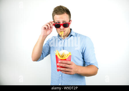 Lustig junge Mann in Rot Brillen mit Pommes frites in seinen Mund auf isoliert weißer Hintergrund Stockfoto
