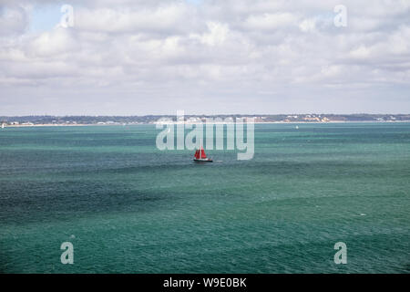 Segelyacht mit roten Segeln geht auf das türkisfarbene Meer, Ärmelkanal, Vereinigtes Königreich Stockfoto