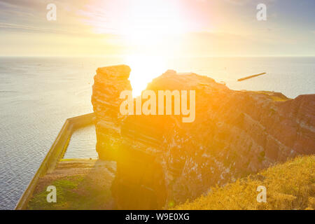 Die roten Sandsteinfelsen der deutschen Insel Helgoland mit der Formation "Lange Anna im warmen Abendlicht. Stockfoto