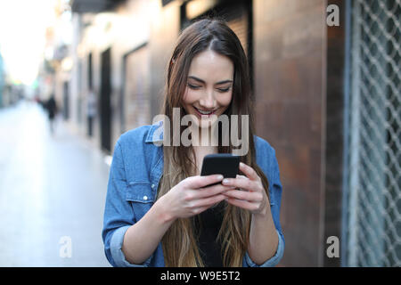 Vorderansicht Portrait Of Happy girl Walking und Kontrollen smart phone auf der Straße Stockfoto