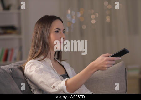 Ernsthafte Frau Fernsehen mit Fernbedienung in der Nacht auf einer Couch zu Hause sitzen Stockfoto