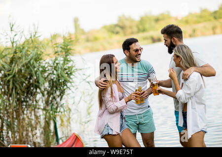 Eine Gruppe von Freunden mit Cider Flaschen stehend durch die Yacht in der Nähe des wunderschönen Sees und Spaß im Sommer Stockfoto