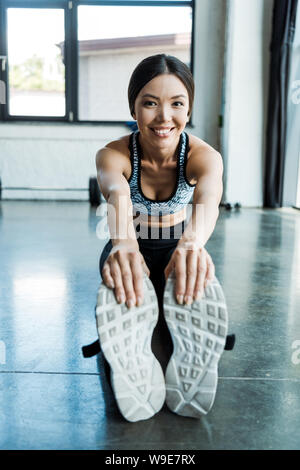 Selektiver Fokus der jungen Sportlerin Stretching und lächelnd im Sportzentrum Stockfoto
