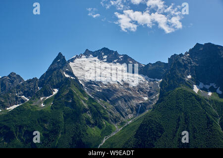 Berggipfel mit einem Gletscher und der Beginn einer Mountain Stream, fließt durch einen Pinienwald. Nördlicher Kaukasus, Russland Stockfoto