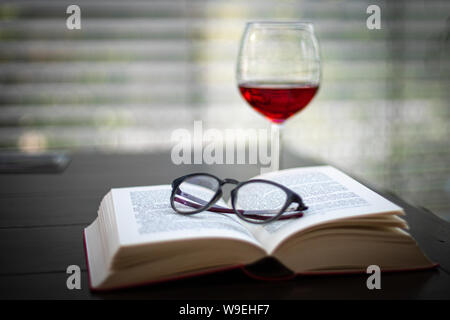 Ein paar Gläser liegt auf einem offenen Buch und im Hintergrund ist ein Glas Wein Stockfoto