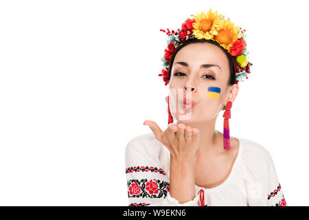 Brünette junge Frau in der Nationalen Ukrainischen bestickt Shirt und floral Wreath blasen Küssen isoliert auf weißem Stockfoto