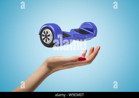 Weibliche Hand mit Blau hoverboard oben auf blauem Hintergrund Stockfoto