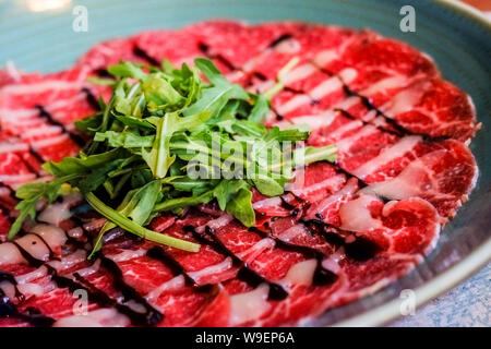 Weiße Schale mit Carpaccio vom Rind auf Rucola in blauen Platte im Restaurant. Traditionellen italienischen Carpaccio vom Rind, selektiven Fokus. Stockfoto