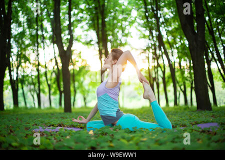 Dünne brünette Mädchen spielt Sport und führt Yoga in einem Sommer Park stellt auf einen Sonnenuntergang Hintergrund. Frau Übungen auf der Yogamatte. Sommer Wald. Stockfoto