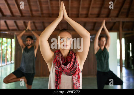 Schöne Lehrerin geben Yoga Klasse in zwei gemischten Rennen Männer auf Yoga Matten in traditionellen Tempel auf Bali, Indonesien Stockfoto