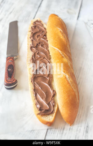 Die Hälfte der Baguette mit Schokoladencreme auf dem hölzernen Tisch Stockfoto