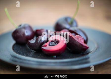 Frische Kirschen auf einer schwarzen Platte, einige in der Hälfte, einige mit Stielen. Stockfoto