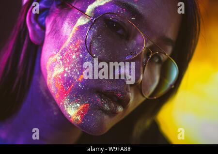 Schöne junge Frau tanzen und Party mit fluoreszierenden Malerei auf ihrem Gesicht. Neon Gesichtsbehandlung Porträts Stockfoto