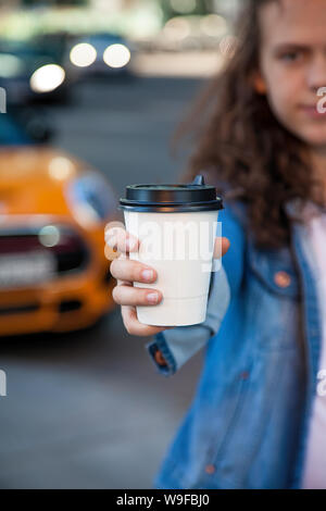 Hand mit einem Drink mit Kaffee im Pappbecher auf dem Hintergrund einer großen Stadt Stockfoto