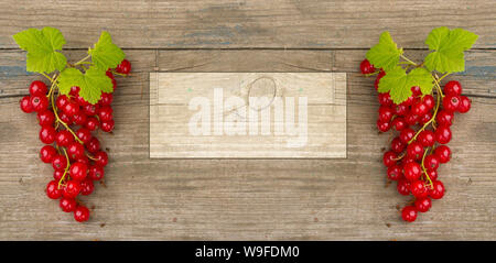 two branches with red currant berries on the sides of a rectangular frame for writing text. Berry composition on old wooden Board Stockfoto