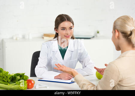 Lächelnd Ernährungsberater im weißen Mantel an Patienten in Tabelle suchen Stockfoto