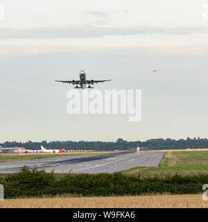 Ein Flugzeug hebt ab, wie andere in Land in einem Flugzeug Landung Warteschlange hinter kommen, mit anderen Ebenen neben der Landebahn zu Abflug warten. Stockfoto